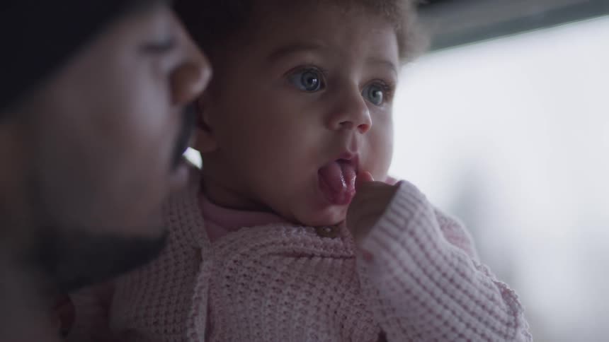 Infant puts its thumb in its mouth while being held by its father