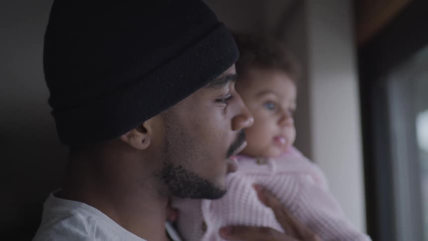 A man holds his infant daughter next to a window for her to look outside