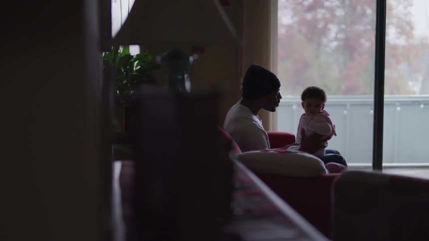 A father sits on a couch while holding his infant daughter on his lap