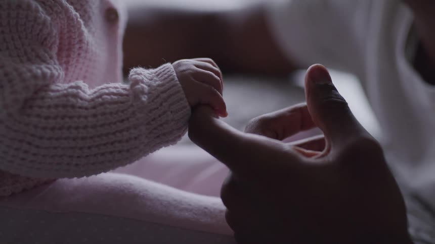A young baby grasps tightly while holding onto her fathers finger