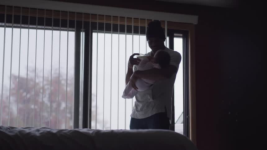 A man with a hat holding a baby and a bottle in a bedroom
