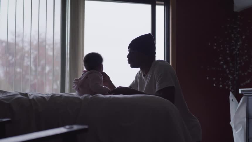 Father sits in front of baby daughter on bed and gently touches her cheek