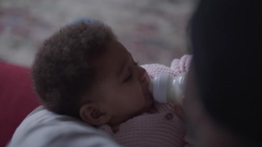 A person holds a baby and feeds her a bottle