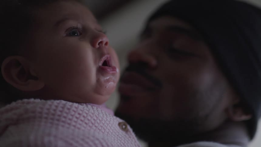 A father holds his chubby cheeked baby daughter who is drooling and fussy
