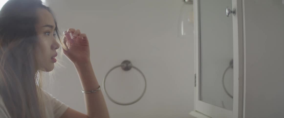 Woman runs hands through hair then reaches out to touch bathroom mirror