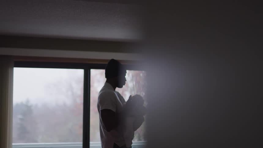 Father rocking baby to sleep near large window indoors