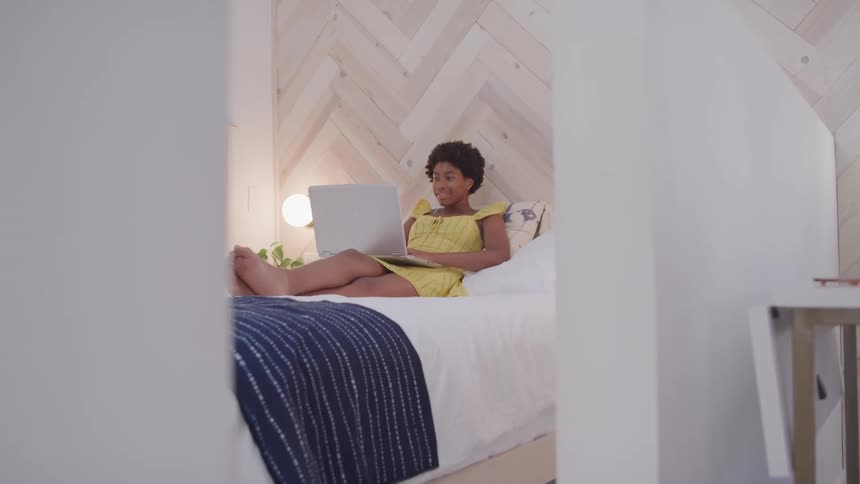 Woman half reclines on bed with laptop on her lap
