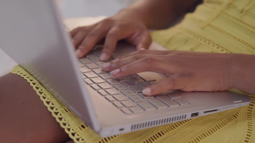 Woman with a yellow dress sits and types on a grey laptop