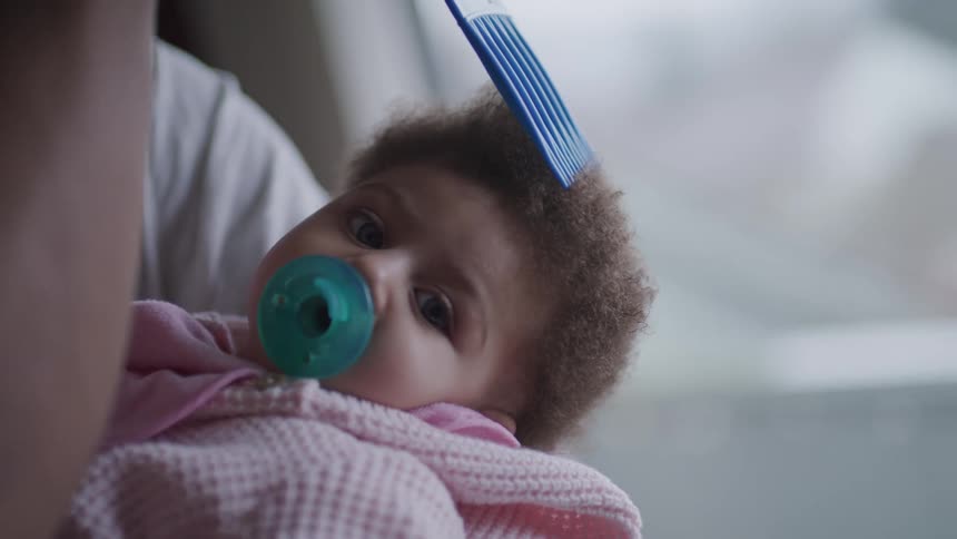 An adult gently picks the hair of a baby being held in their arms