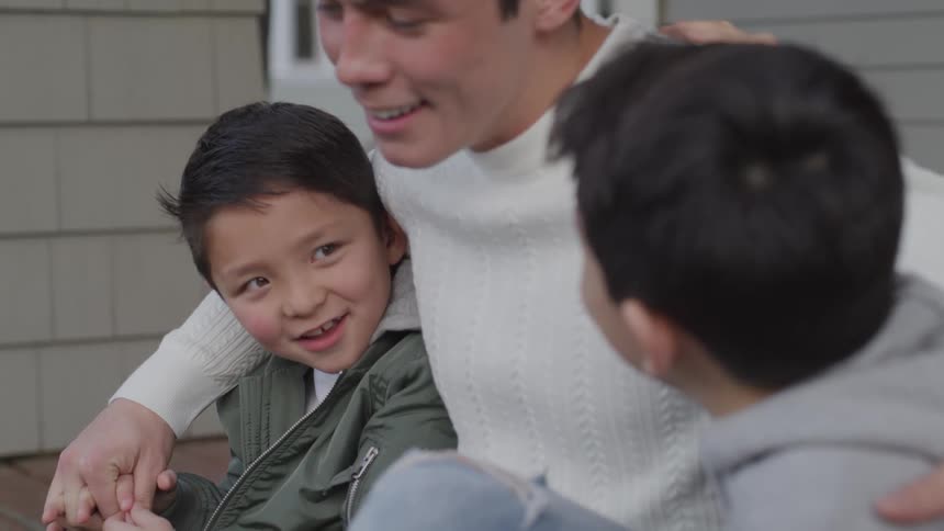 A man and two boys sitting on a porch with a house and a window in the background