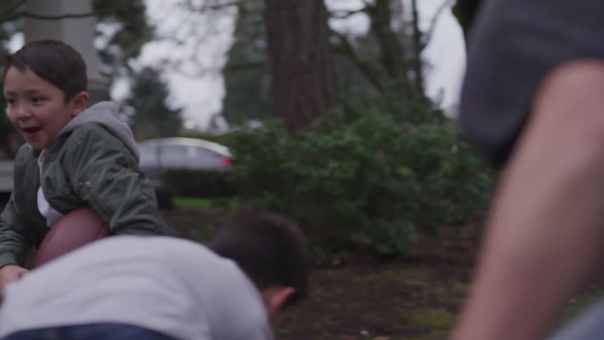 Boy in yard near house runs with football while others try to grab him