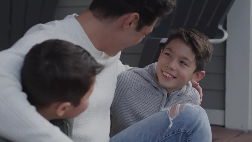 A man sitting outside with his home talks with his sons