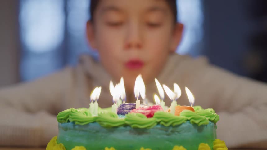 Boy makes a wish and smiles before blowing out the burning candles on a round birthday cake
