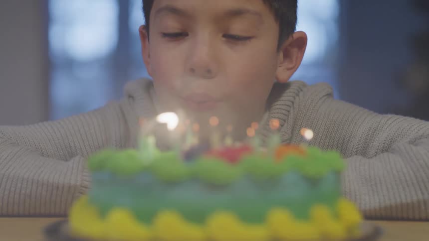 A young boy takes a deep breath in and blows out candles atop a birthday cake
