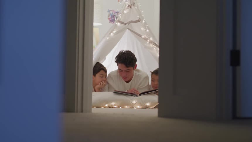 Father reading to his kids under a lighted tent in their bedroom