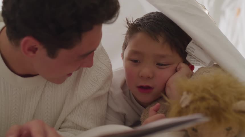 A teenage boy lies in a tent with his younger brother and reads to him