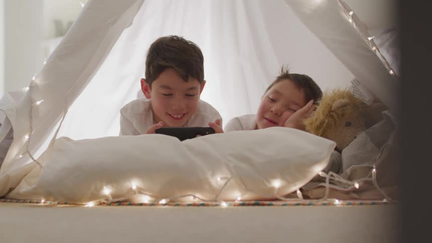 Two boys plays a game on cell phone in a fort at home