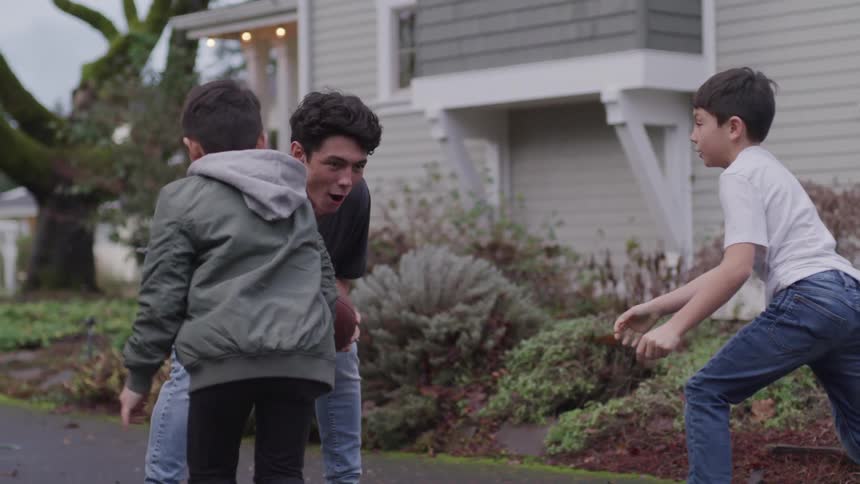 A teenager boy is tackled by his younger brothers as they play football outside their home