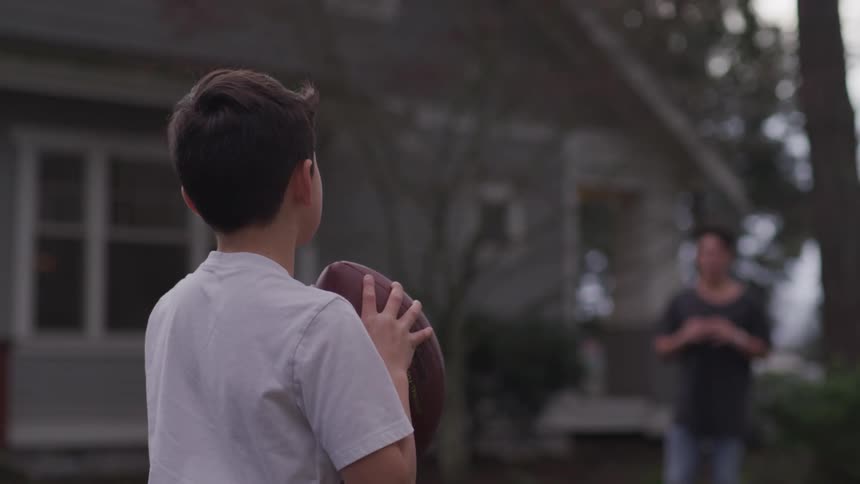 A young boy throws a football to his older brother outside their house
