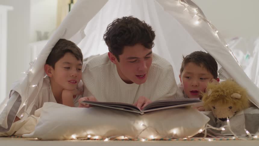 Three brother lay inside of a home made tent reading a book