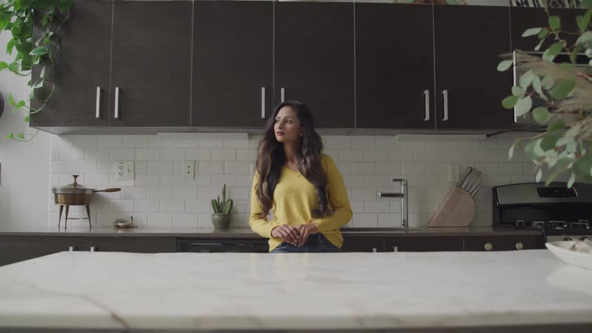 A woman stands quietly in her kitchen looking off into the distance