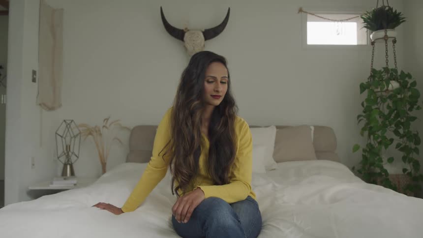 A woman sits on her bed with a smile on her face