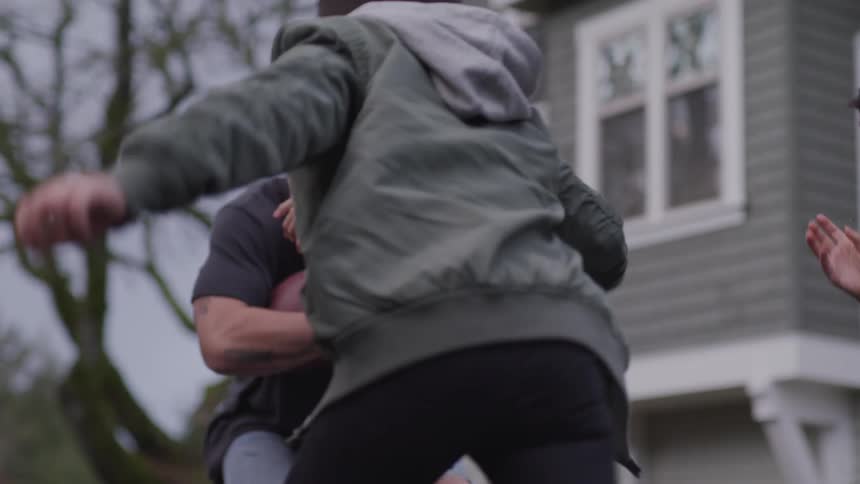 Two brothers tackle their older brother as they all play football outside their home