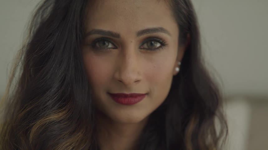 Brunette woman with wavy hair and earrings faces the camera with eye contact