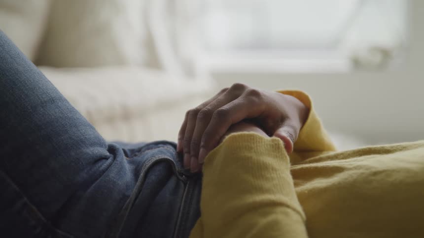 Woman with jeans and a yellow sweater lying down on bed puts her hands on her stomach
