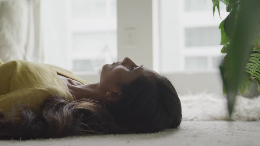 Brunette woman with wavy hair and a yellow sweater lies on a white carpet in the living room