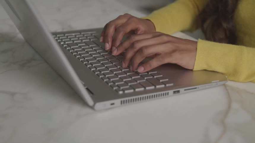 Brunette woman with a yellow sweater uses a grey laptop