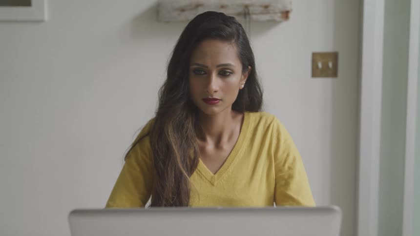 A woman with lipstick and a yellow sweater sitting in front of a laptop