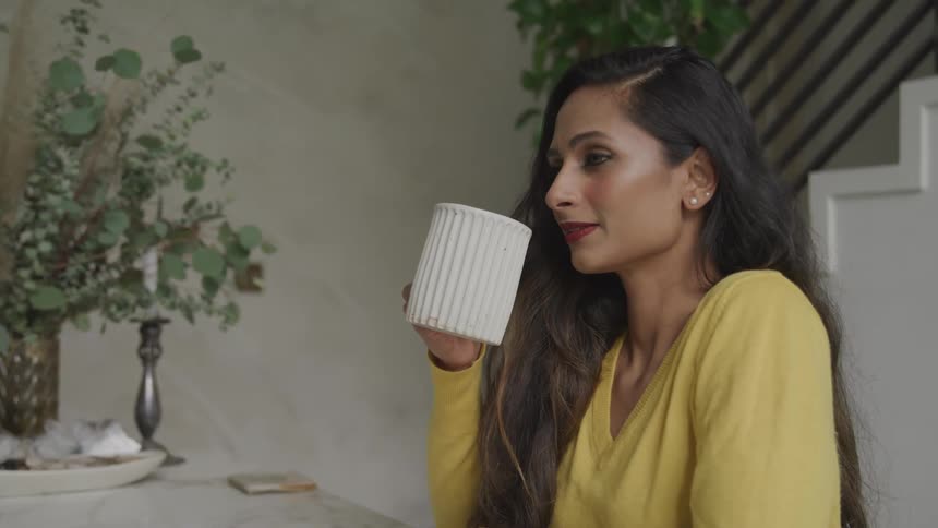 A woman sitting at home drinks a cup of coffee