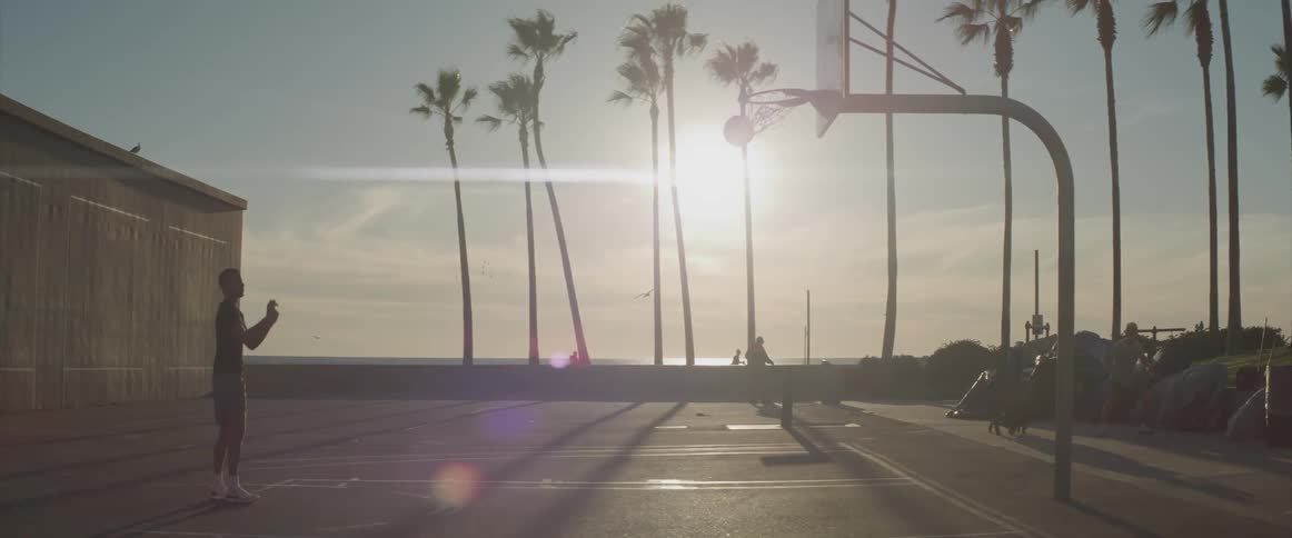 A boy shoots a basketball on a court near some palm trees