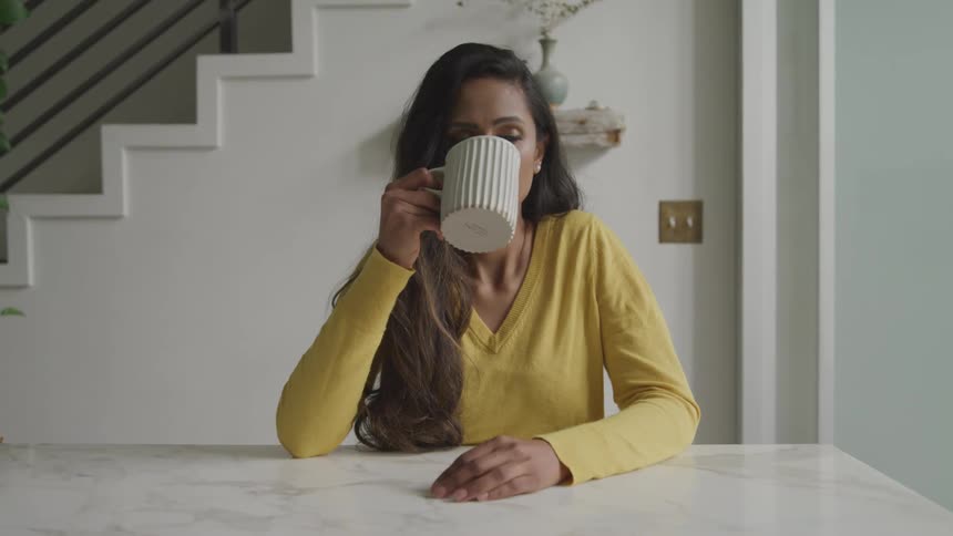 A woman slowly takes a drink from a very large mug and then smiles subtly