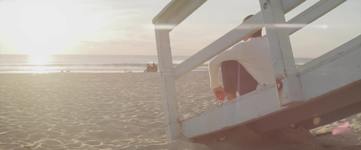 A man watches the sun rise while sitting on a ramp to a lifeguard station at the beach