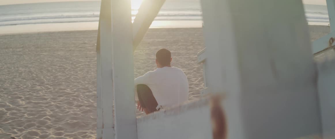 Man sits near wooden staircase looking out to sea as others walk closer to water