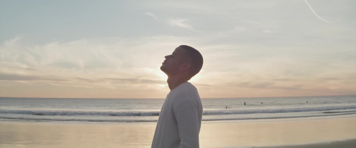 Silhouette of a young man standing on the sand beach at sunset next to the ocean