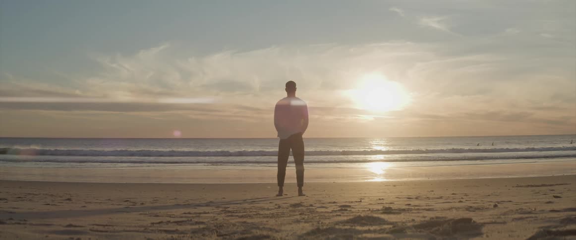 Man standing on the beach looking out to the horizon at sunset