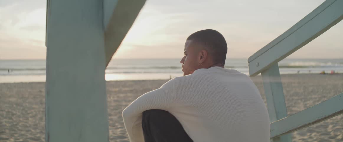 A young man is sitting on a wooden ramp on the beach