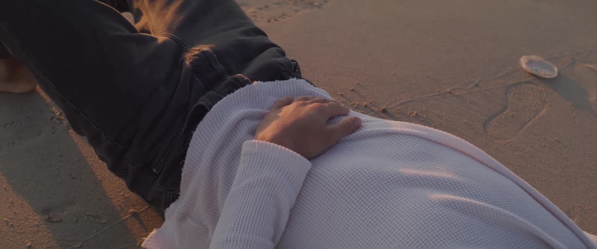 Person wearing pants and a long sleeve shirt rests on sand