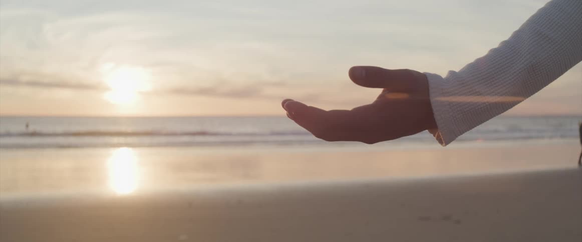 Arm reaching out with the palm facing up while on a beach near the ocean