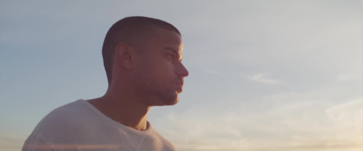 Man with a white sweatshirt walks on the wet beach next to the sea at sunset
