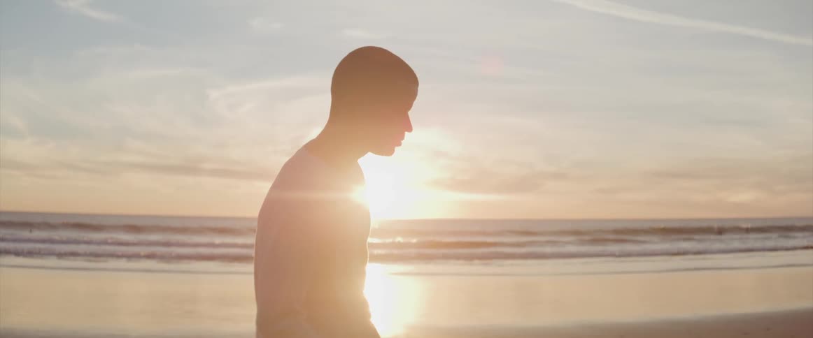 A man is walking on the beach at sunrise