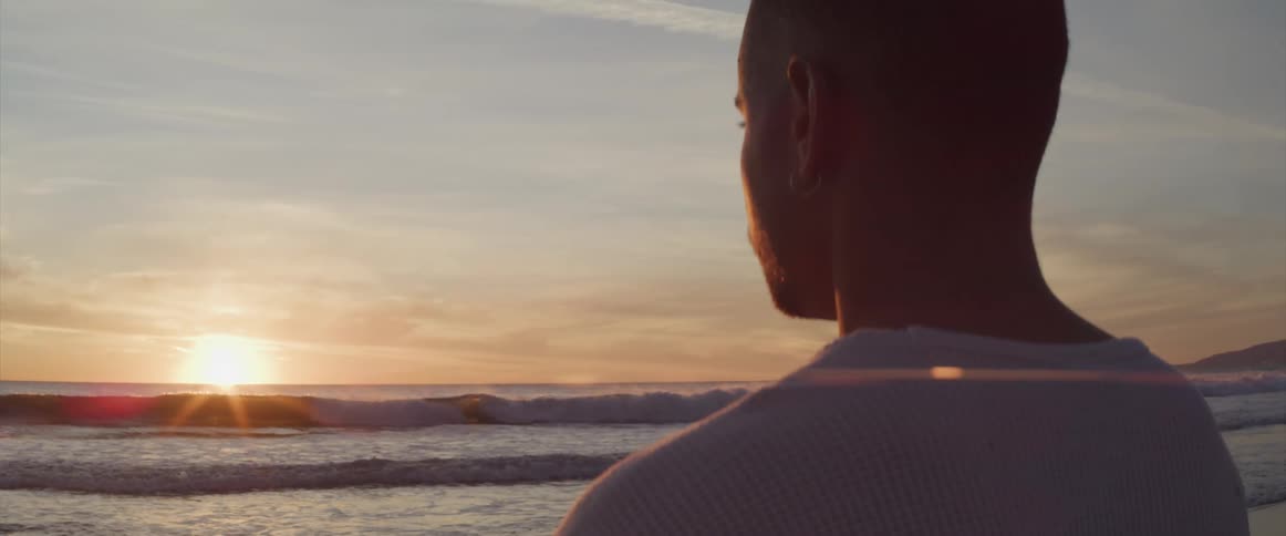 Man looks out toward sun sitting on horizon over ocean