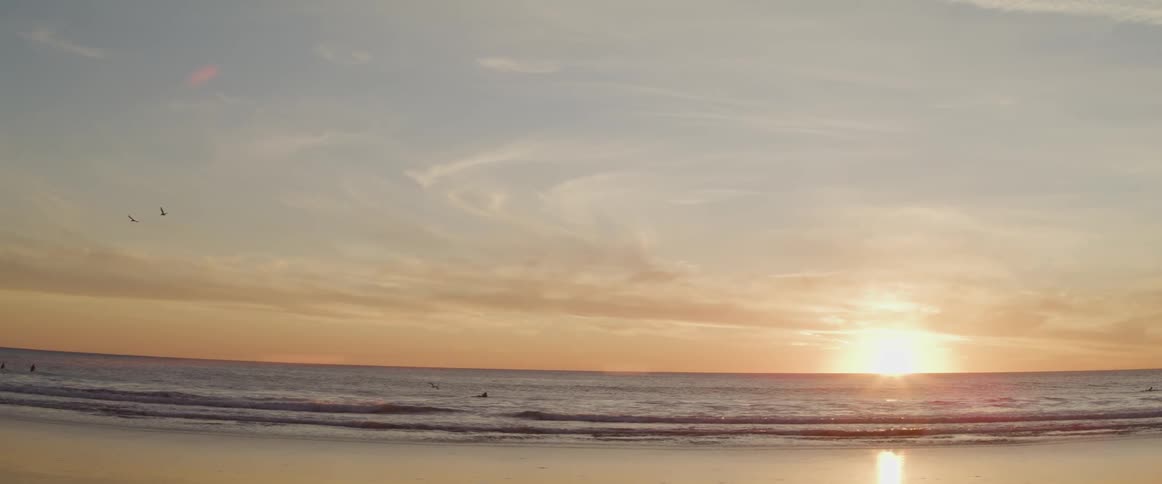 The sun is set very low in the sky over a sandy ocean beach