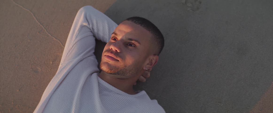 Man with a white sweatshirt lies on the beach at sunset next to the sea