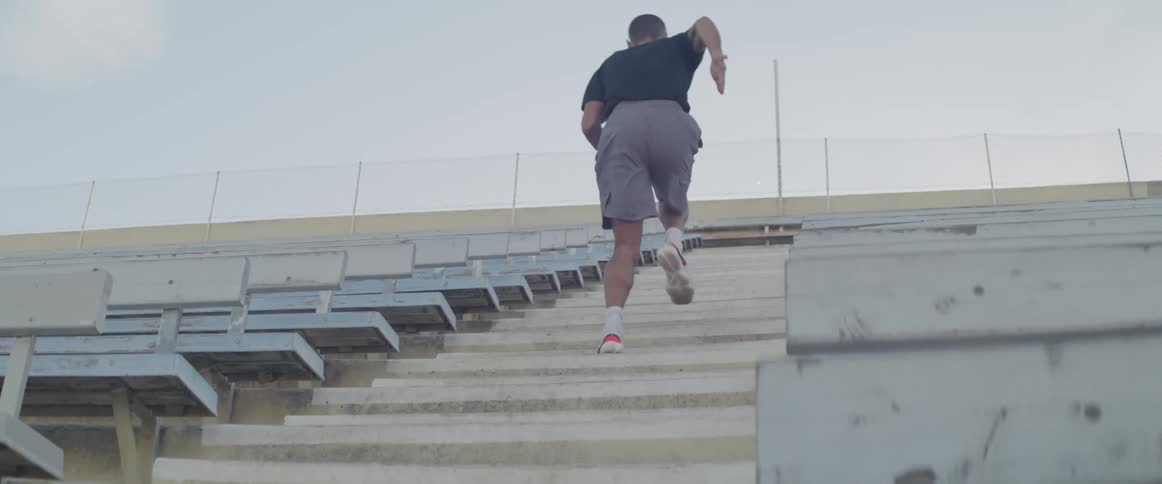 A man runs up a staircase in the empty stands of an athletics field
