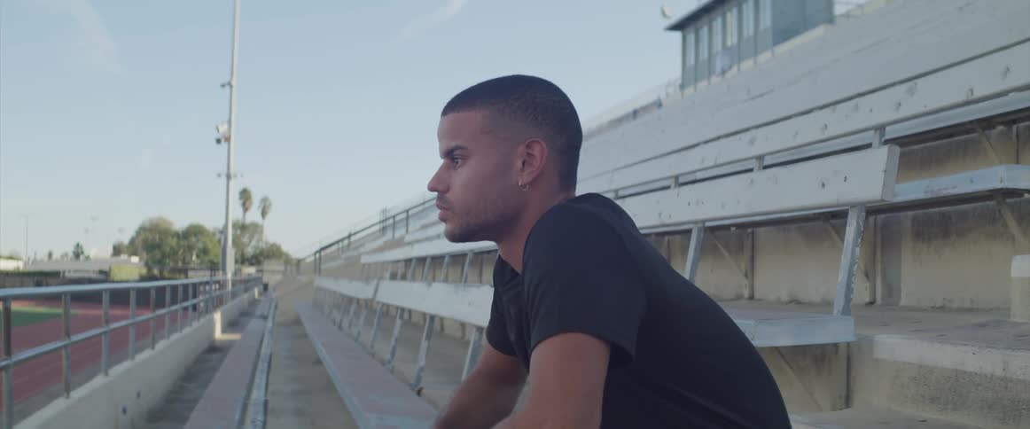 Man sits on stadium seat alone looking down as he contemplates sports field