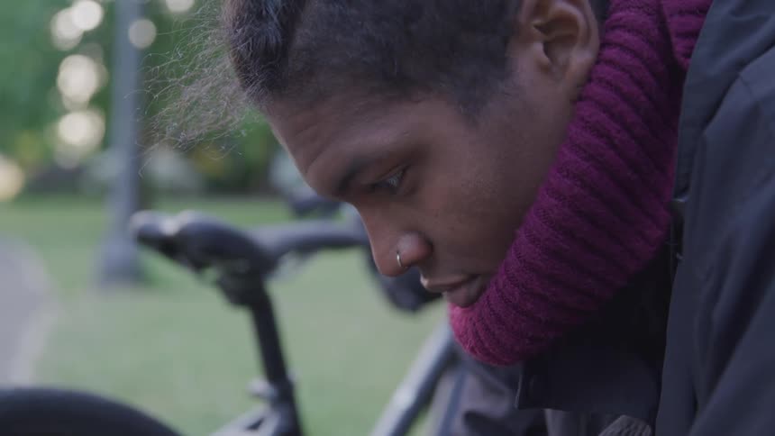 A man with a turtleneck sitting with a bike grass and trees in the background